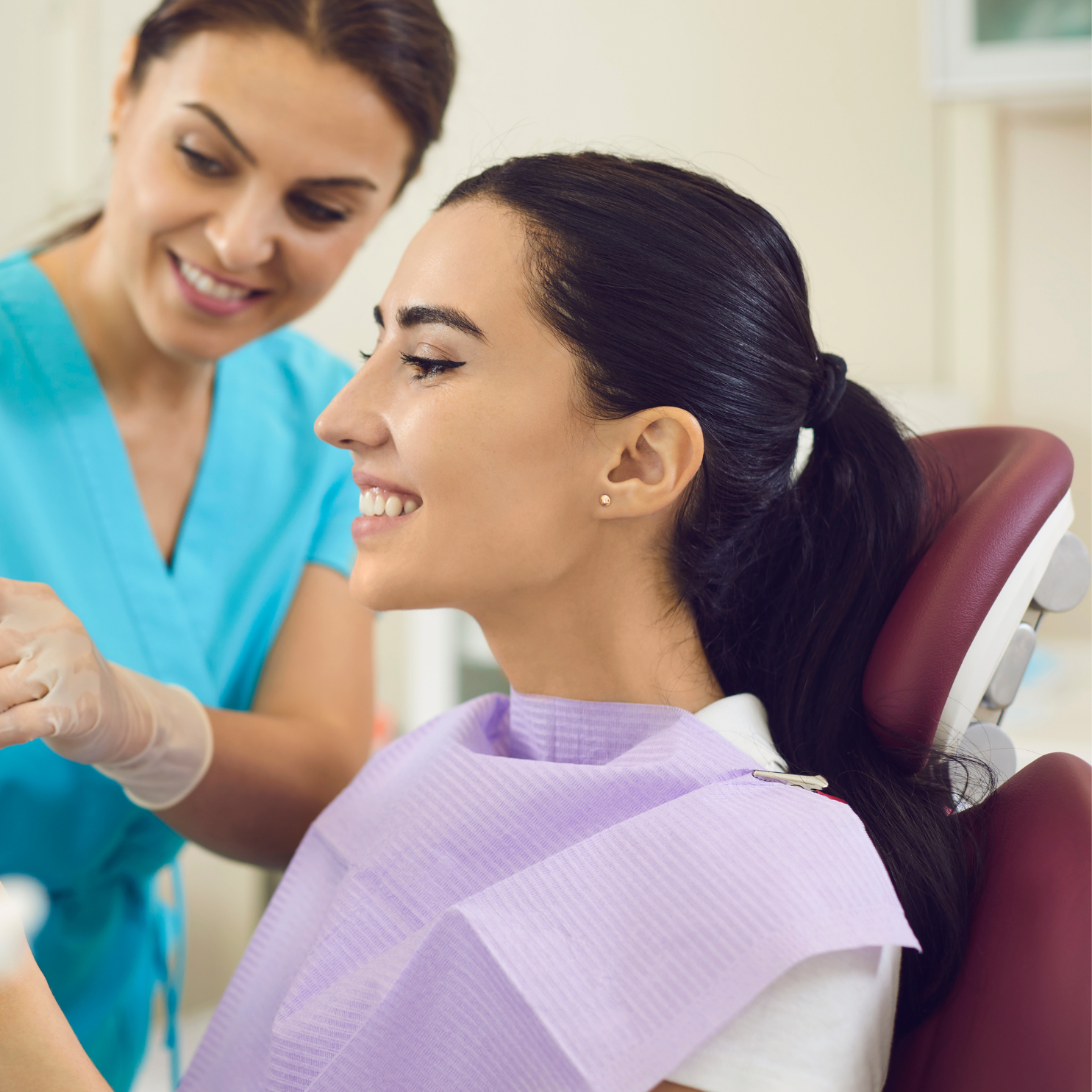 Smiling female dental hygienist standing next to a patient seated in the treatment chair