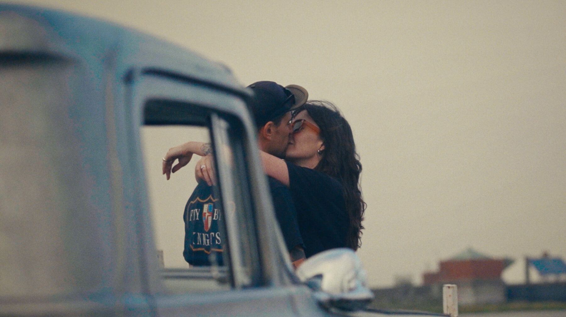 Couple embracing and kissing near a vintage blue car at dusk.