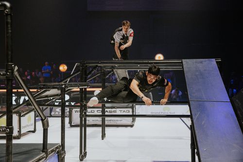 2 athlète de chase taf s'affontant sur le terrain . le chaser est en hauteur prêt à descendre sur l'evader. la scène prend place dans un centre commercial au milieu de spectateurs