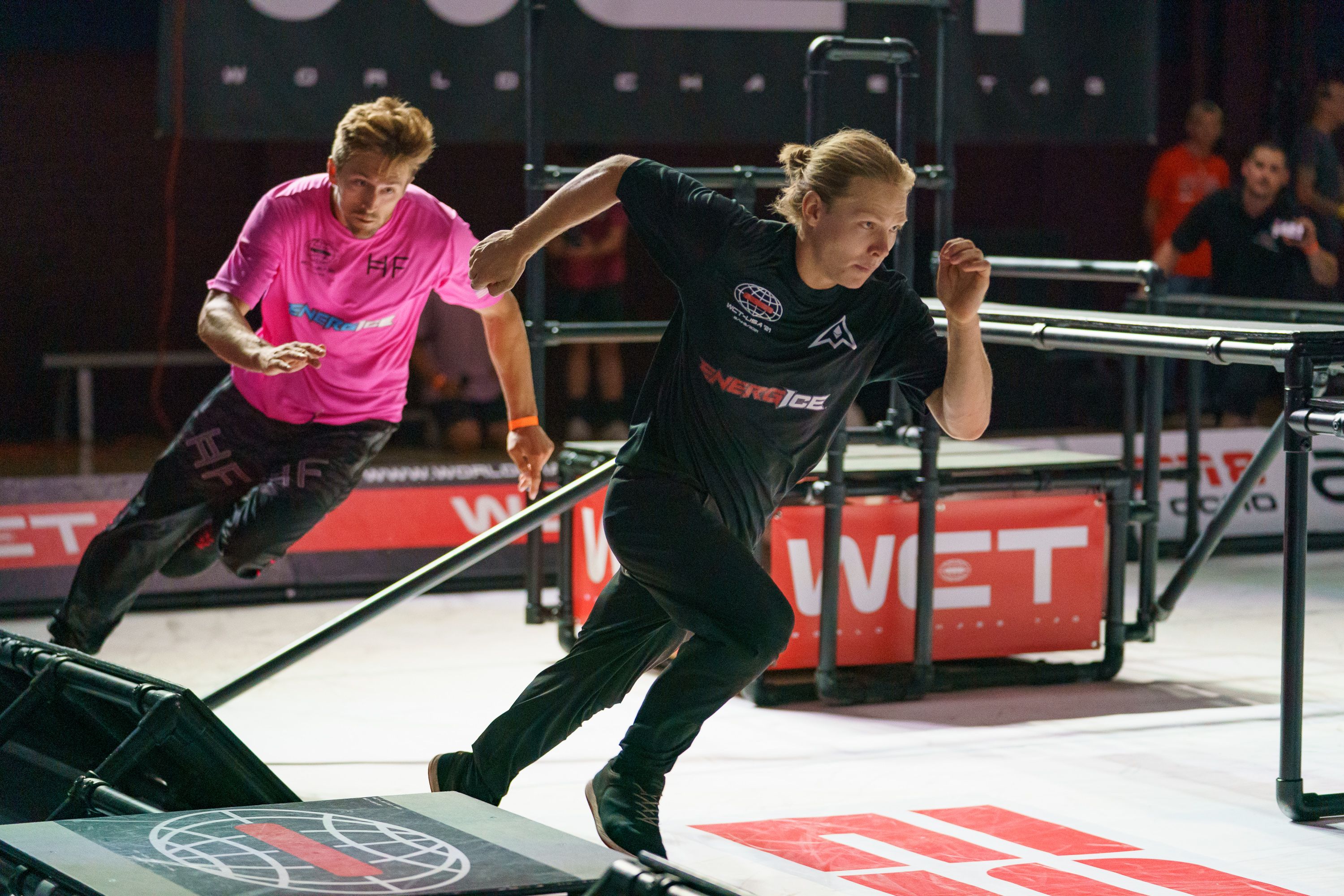 2 athlète de chase taf s'affontant sur le terrain . le chaser est en hauteur prêt à descendre sur l'evader. la scène prend place dans un centre commercial au milieu de spectateurs 