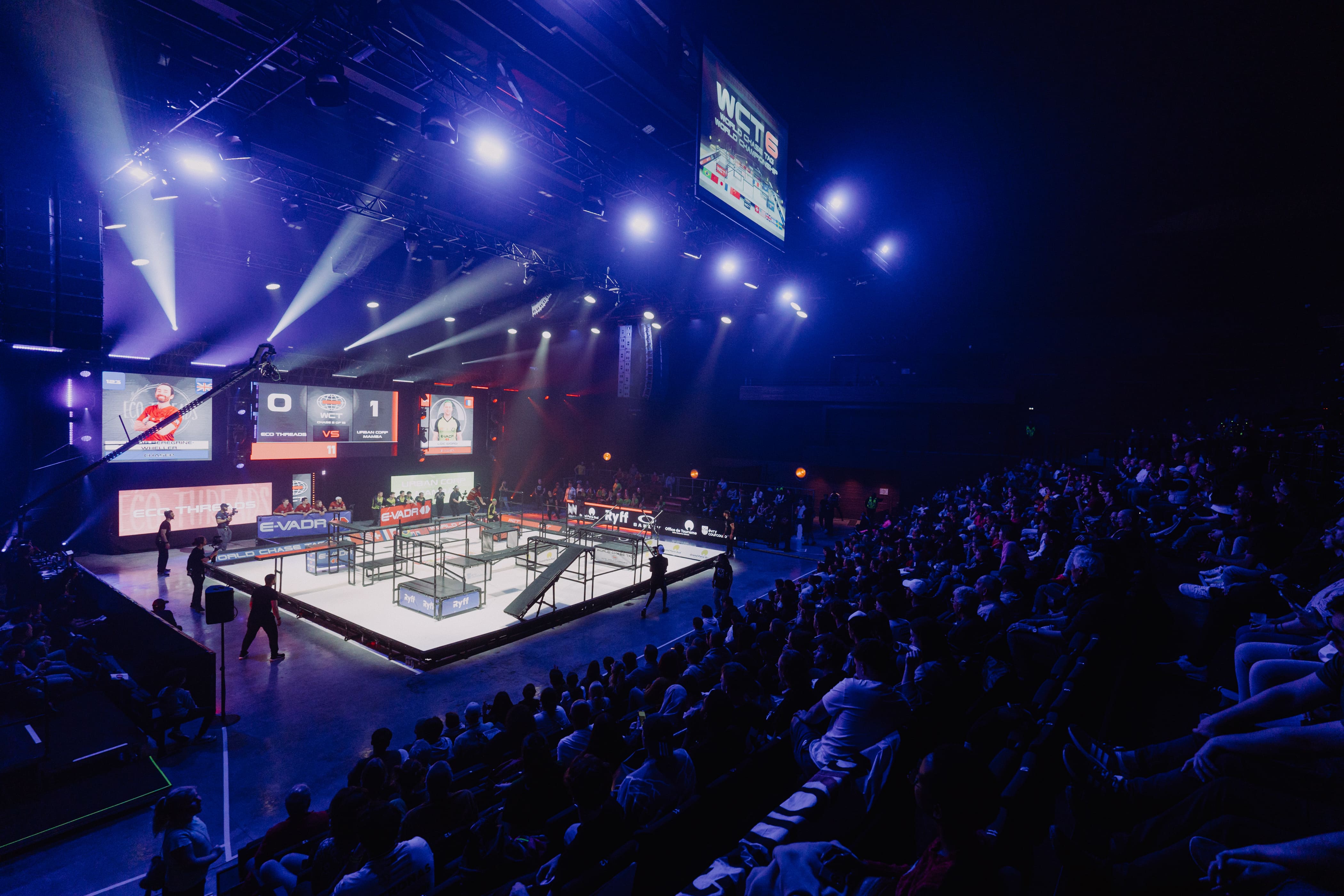 2 athlète de chase taf s'affontant sur le terrain . le chaser est en hauteur prêt à descendre sur l'evader. la scène prend place dans un centre commercial au milieu de spectateurs 