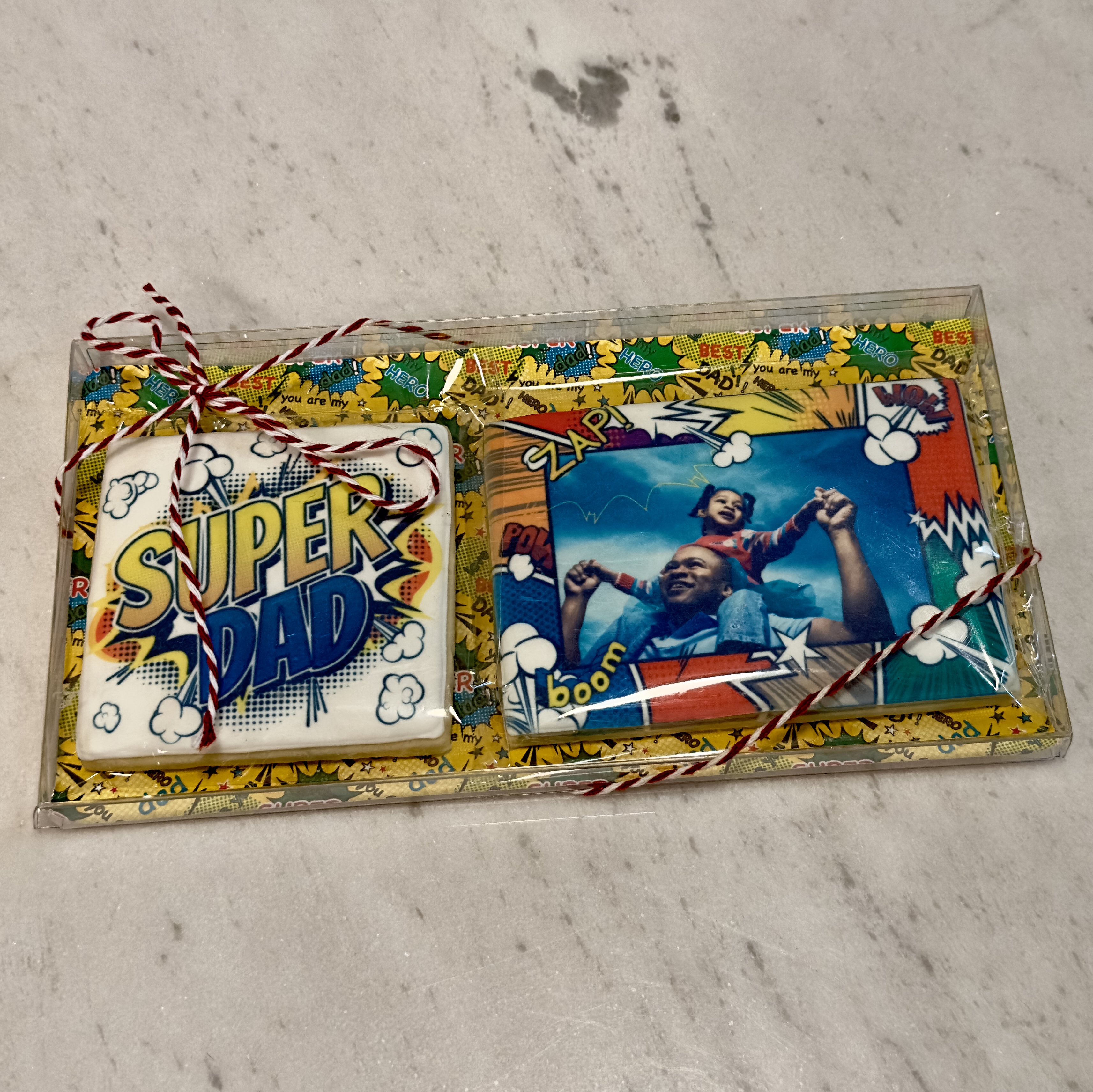 Set of 2 Big Cookies - 1 Super Dad (3" square) + 1 Hero Frame with a Custom Photo (4.5"x3") in a gift clear box with super dad backer and twine.
Each cookie is individually wrapped in a heat-sealed cello bag for freshness.