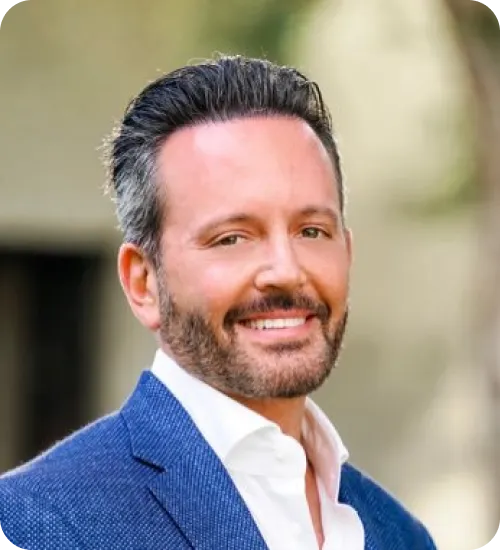 Smiling man with neatly styled dark hair and beard, wearing a blue blazer and white shirt.