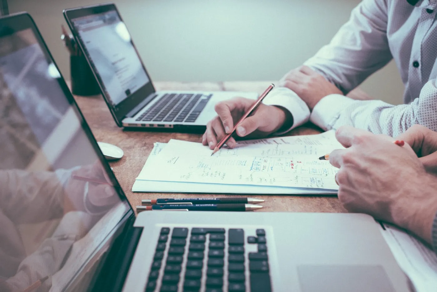 Two people collaborate on a paper with pen in hand and each has a laptop open.