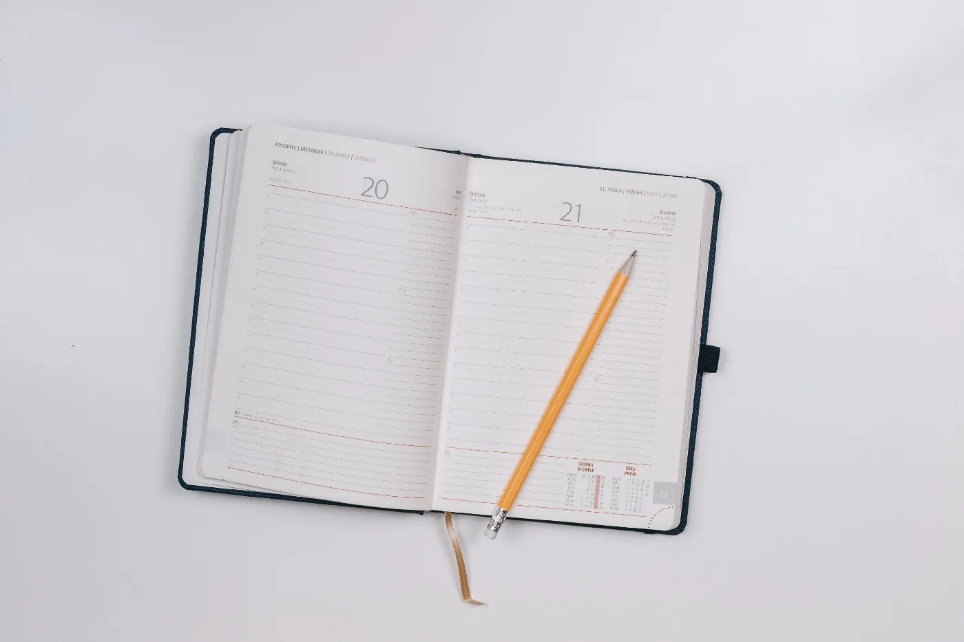A pencil rests on an empty appointment book, which is opened to a blank page.
