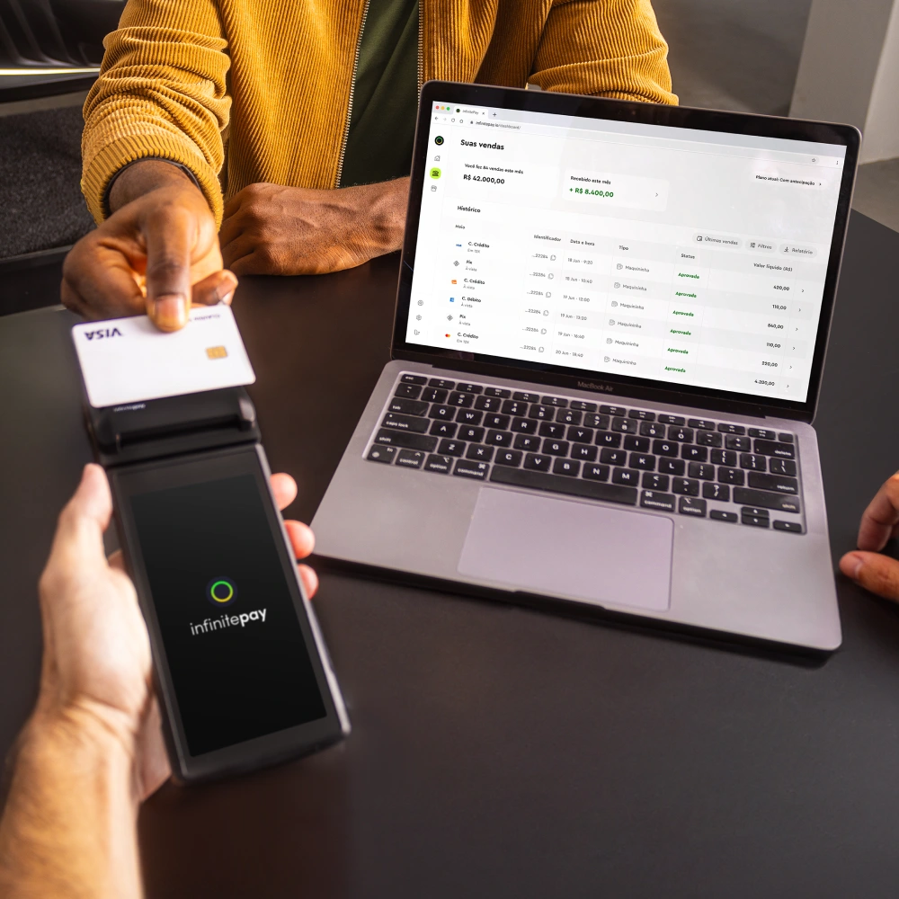 Vendedor usando um boné roxo, olhando para a tela de seu smartphone enquanto utiliza o app InfinitePay em um ambiente decorado com plantas.
