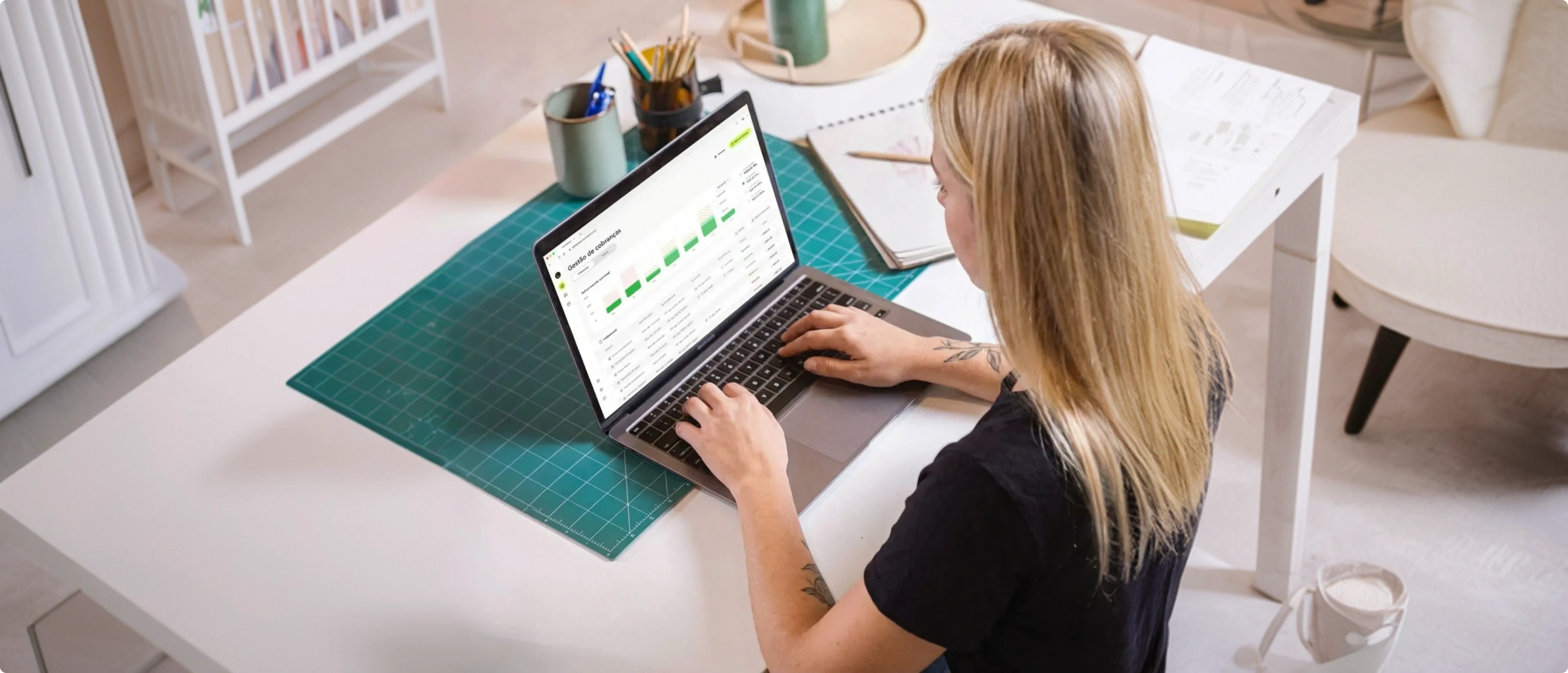 Mulher usando um laptop, gerenciando cobranças com o app InfinitePay em uma mesa de trabalho, cercada por materiais de escritório.