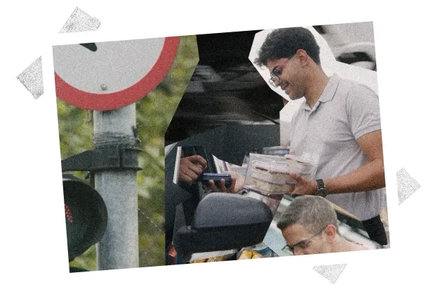 Smiling man in glasses holding food containers and a payment card near a car window.