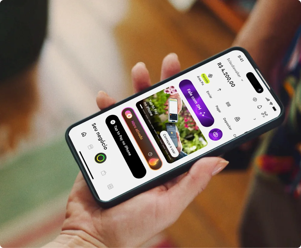 Pessoa segurando um smartphone com o aplicativo InfinitePay aberto. O fundo tem iluminação aconchegante com luminárias e um bar