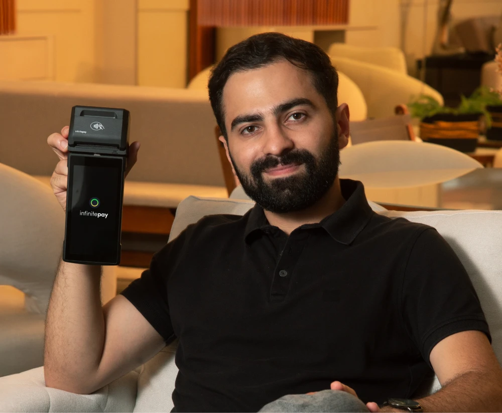Pessoa digitando em uma máquina de cartão InfinitePay, sobre um balcão de pedra, com um bar elegante ao fundo