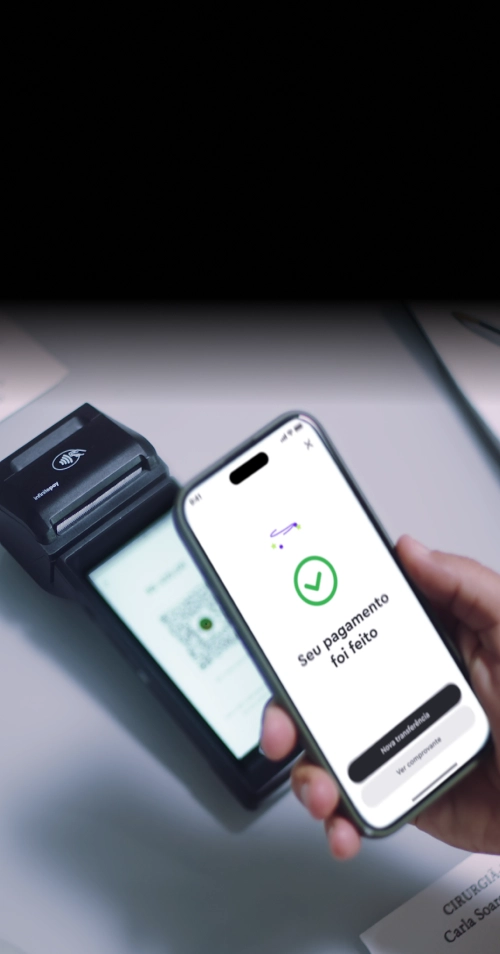 Mulher elegante de terno preto segura uma maquininha InfinitePay em um ambiente sofisticado com iluminação aconchegante.