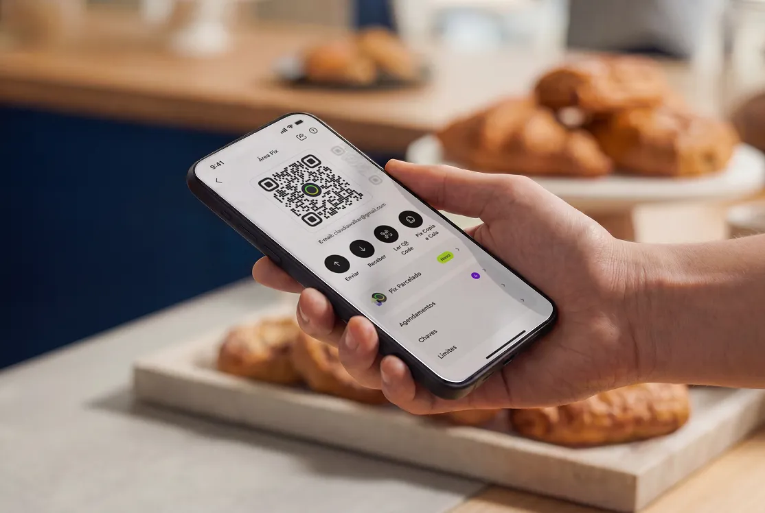 Hand holding phone displaying a PIX QR code for payments with pastries blurred in the background.