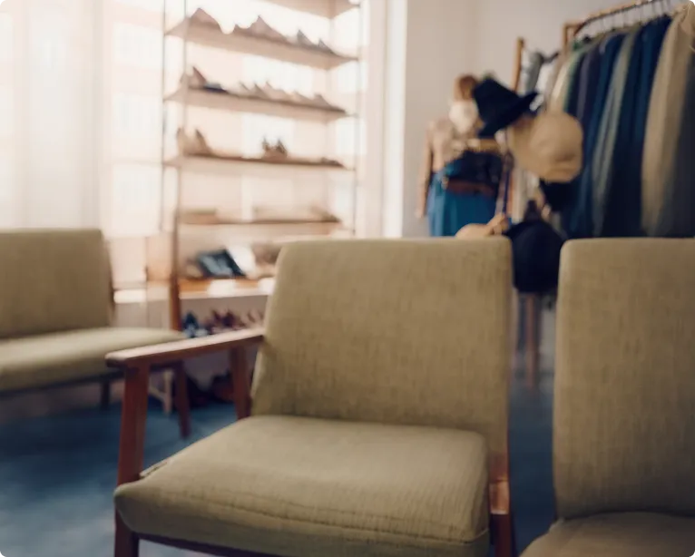 Blurred interior of a clothing store with cushioned chairs, shoe shelves, and hanging clothes.