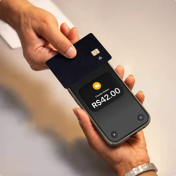 Person holds phone displaying R$42.00 payment while another taps a contactless card on it.