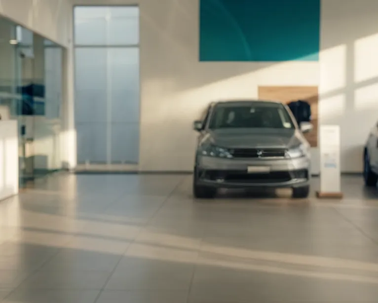 Out of focus view of a car showroom with a grey car in the center and sunlight casting shadows.