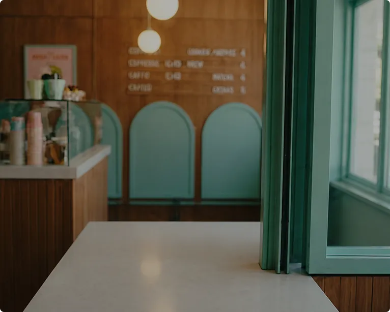 Empty cafe counter with teal window frames and menu on wooden wall in background.