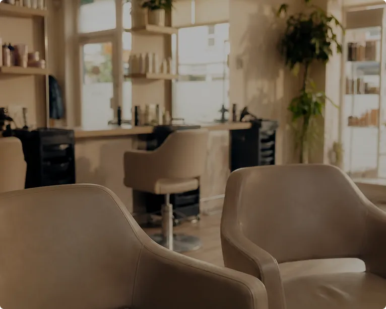 Interior of a cozy salon with brown leather chairs and shelves with hair products by the window.