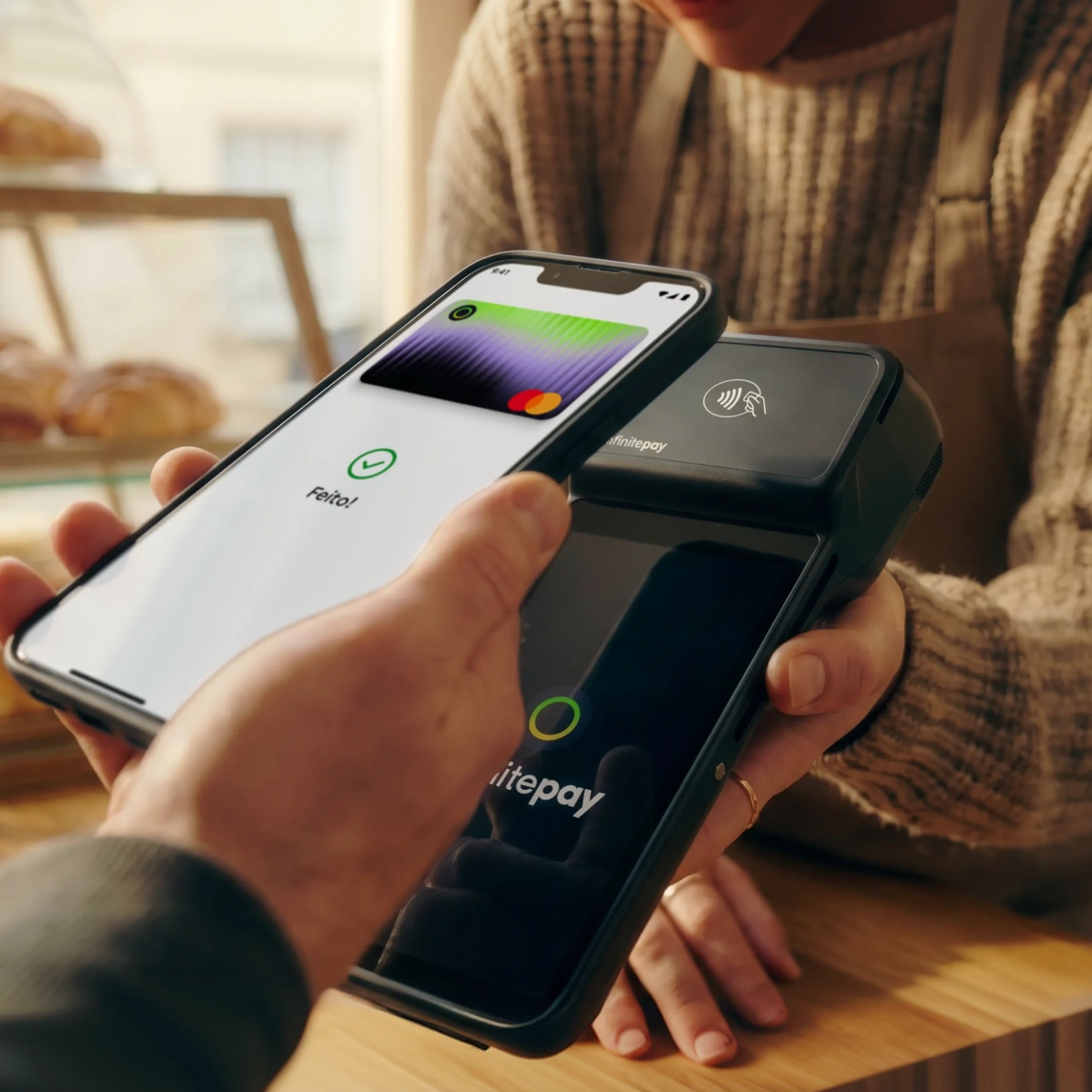 Person holding smartphone with digital card over a payment terminal for contactless payment.