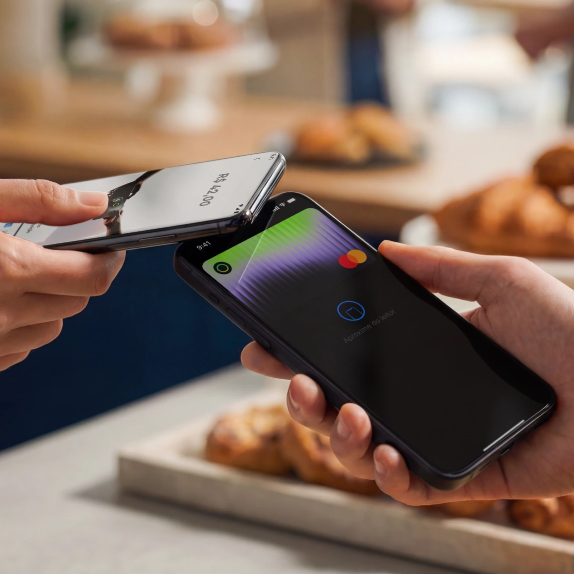 Two hands holding smartphones, one scanning for a digital payment near pastries on a table.