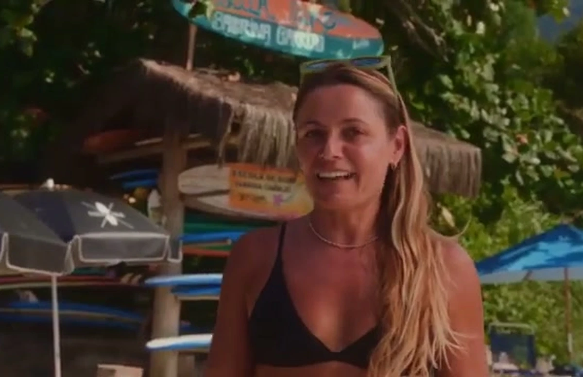Sabrina, da escola de surf, sorrindo em frente às pranchas na praia