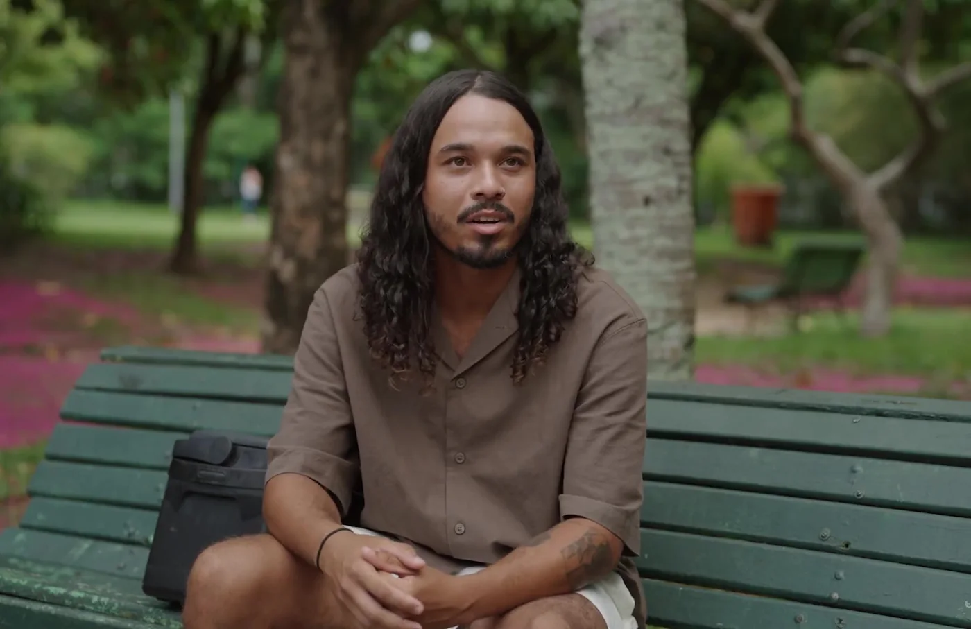 Felipe Marques, vendedor ambulante, sorrindo sentado em um banco de praça arborizada
