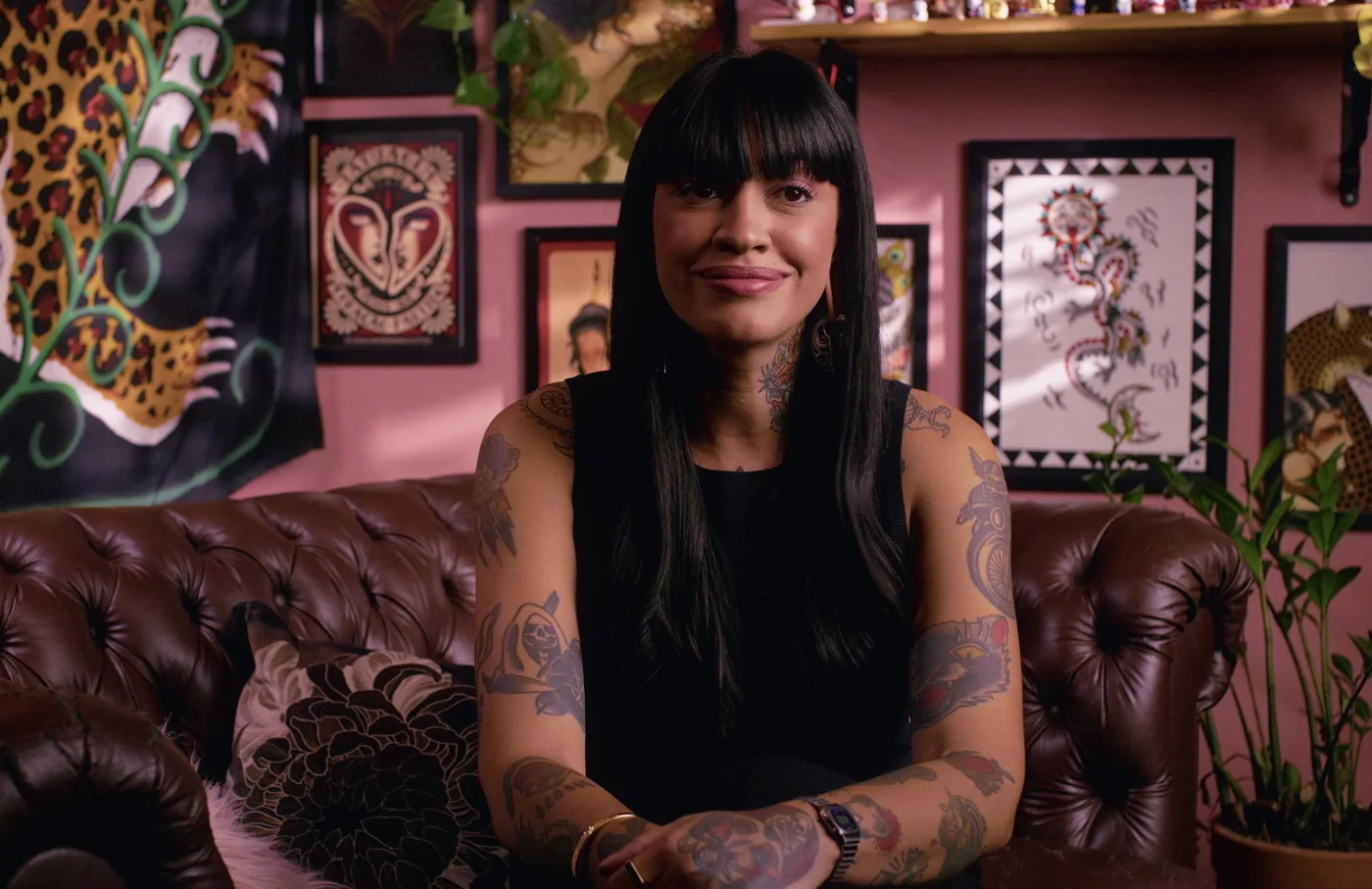 Laila do Amaral, tatuadora, sentada em sofá de couro no seu estúdio de tatuagem