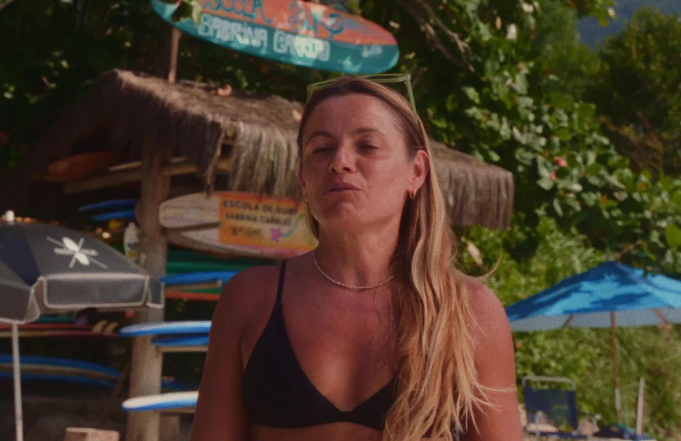 Sabrina, da escola de surf, sorrindo em frente às pranchas na praia