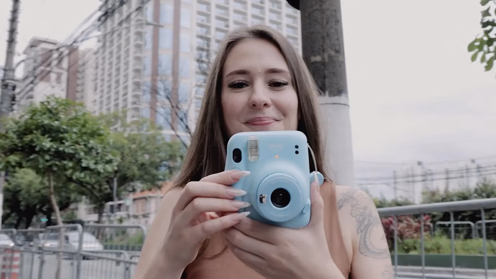 Imagem que ilustra artigo sobre o casal Henrique Gonetecki e Ketlyn Ivanoski mostra ela em primeiro plano segurando uma câmera de fotos instantâneas