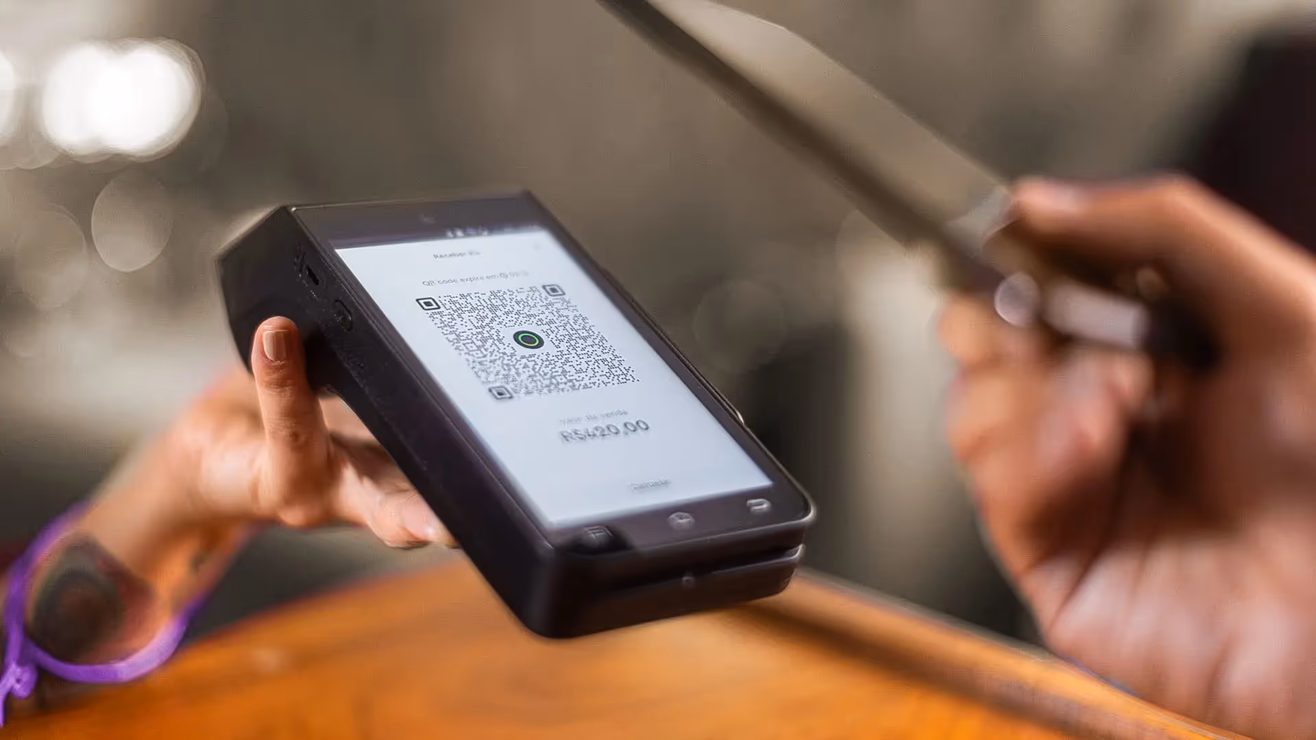 maquininha InfinitePay, a melhor do mercado, com Pix QR Code na tela e celular lendo o código.