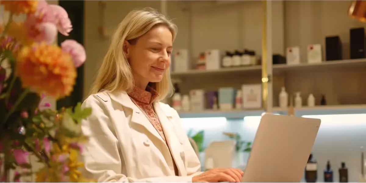 Mulher loira sorridente usando laptop lendo como criar uma loja virtua para sua loja de cosméticos.