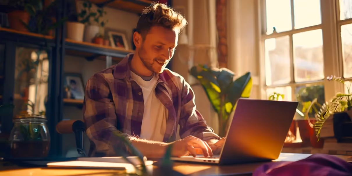 Homem sorrindo enquanto usa um laptop lendo um artigo sobre como fazer sorteio online, em um ambiente iluminado e cercado por plantas.
