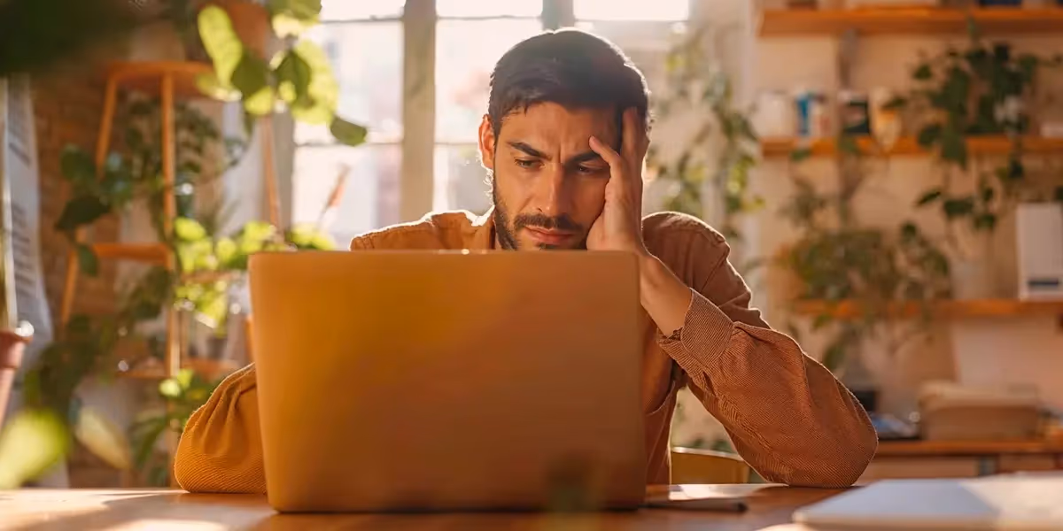 Homem sentado em frente a um laptop, com expressão preocupada, sugerindo análise de comprovante falso do Pix