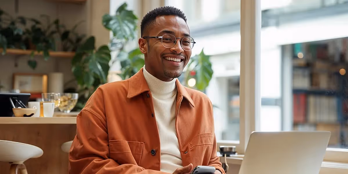 homem em um ambiente de escritório, sorrindo e utilizando seu notebook, pesquisando sobre como vender infoprodutos.