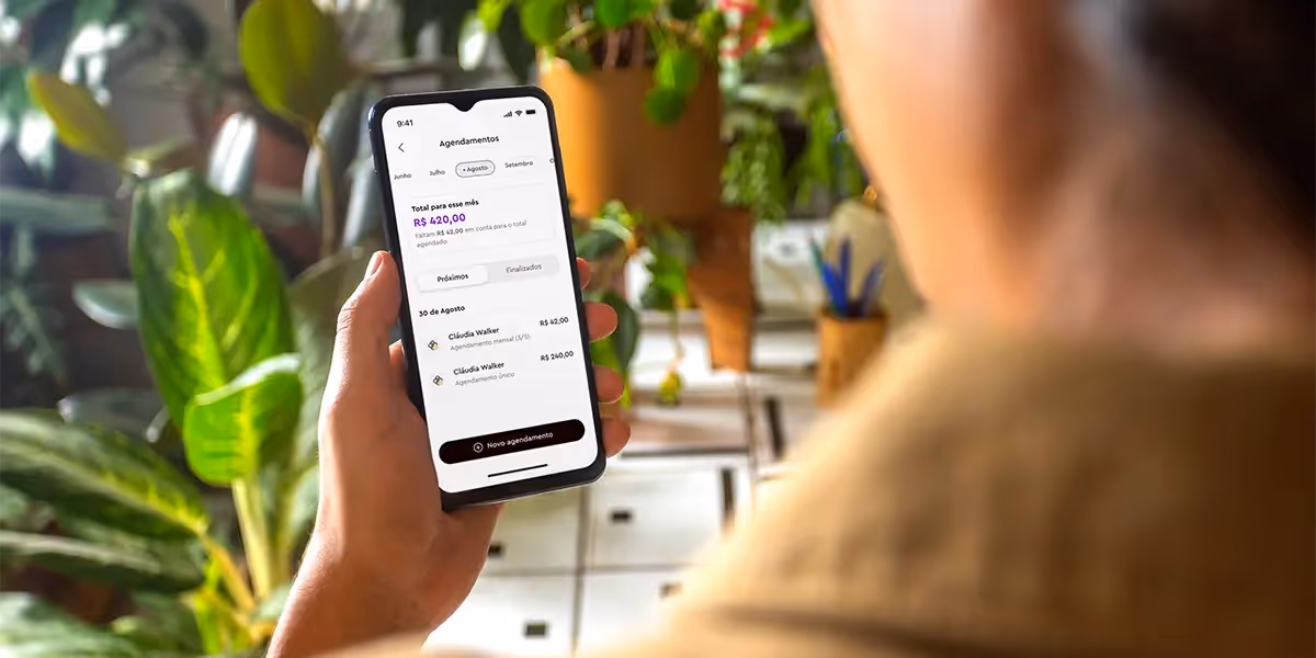 Pessoa segurando um celular exibindo a tela de confirmação de um Pix agendado no valor de R$ 42,00. Ao fundo, há várias plantas em vasos.
