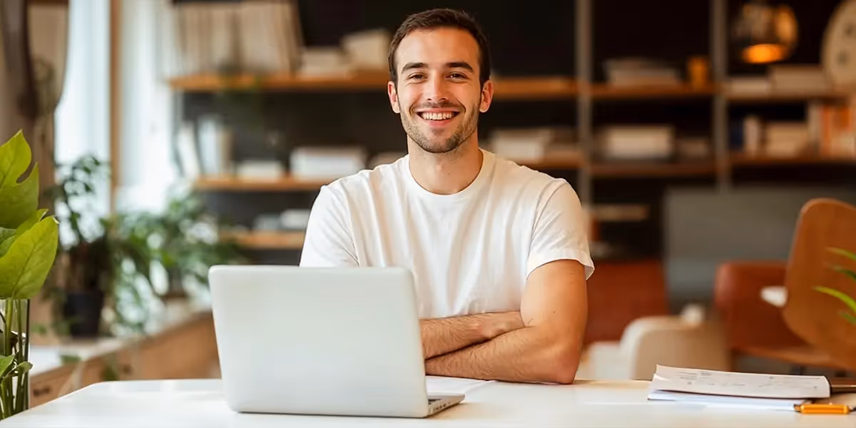 homem sorri para a câmera após ler sobre como regularizar CNPJ. ele está sentado em uma cadeira de escritório com seu notebook apoiado sobre a mesa à sua frente.