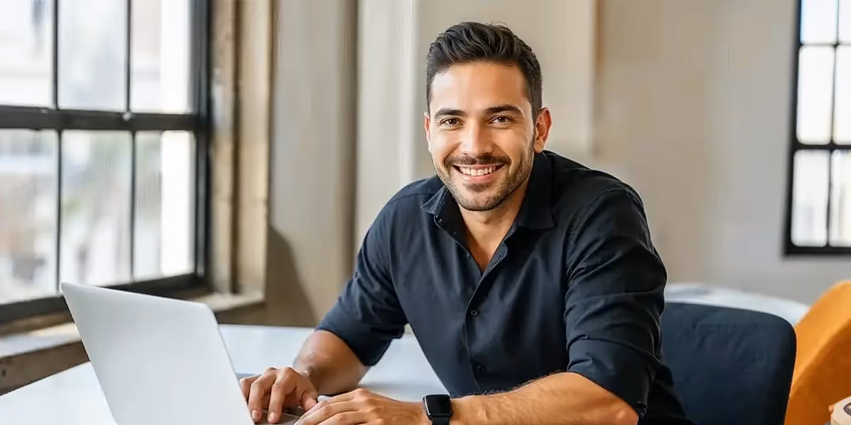 Homem sorridente trabalhando no laptop, analisando dados sobre a Taxa Referencial em um ambiente de escritório moderno
