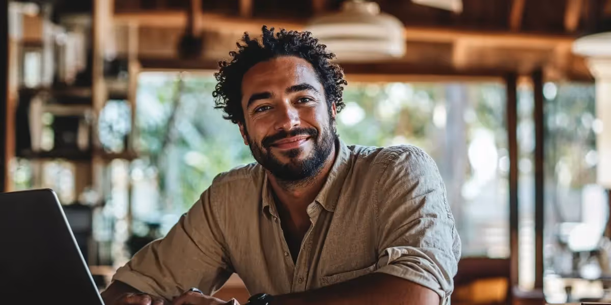 Homem em seu escitório em casa. O ambiente é rústico, com paredes de madeira. ele está sorrindo para a câmera, usando seu notebook. Ele acaba de ler um artigo sobre agenda tributária 2025, para planejar seus negócios.