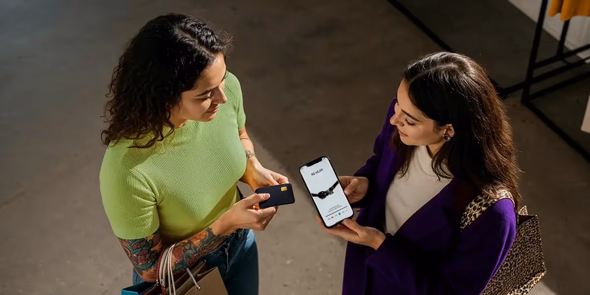 Maquininha de cartão no celular sem taxa sendo usada para receber pagamento por aproximação entre duas mulheres, uma segurando o cartão e outra mostrando o valor na tela do celular