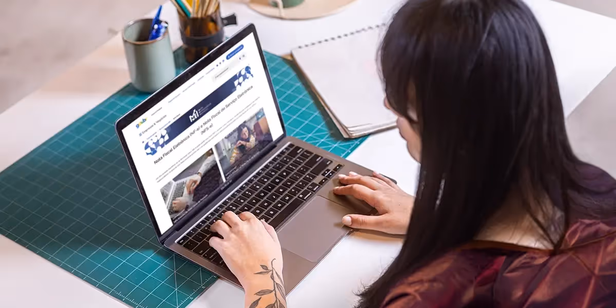 Mulher de frente para um computador com a tela mostrando uma página do site do gov.br simbolizando a busca por "Como emitir nota fiscal avulsa MEI"