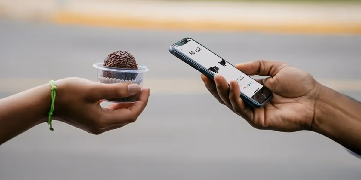 doces para vender na rua sendo pagos via celular por aproximação, com brigadeiro em pote plástico sendo entregue.