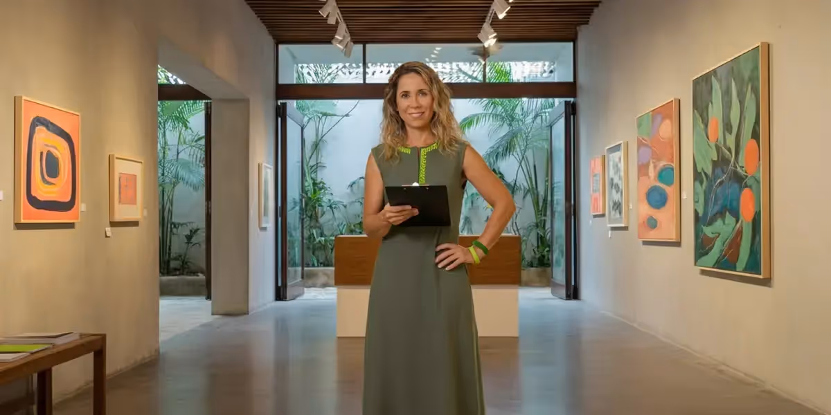 Empresária feminina sorridente em galeria de arte, segurando prancheta e celular.