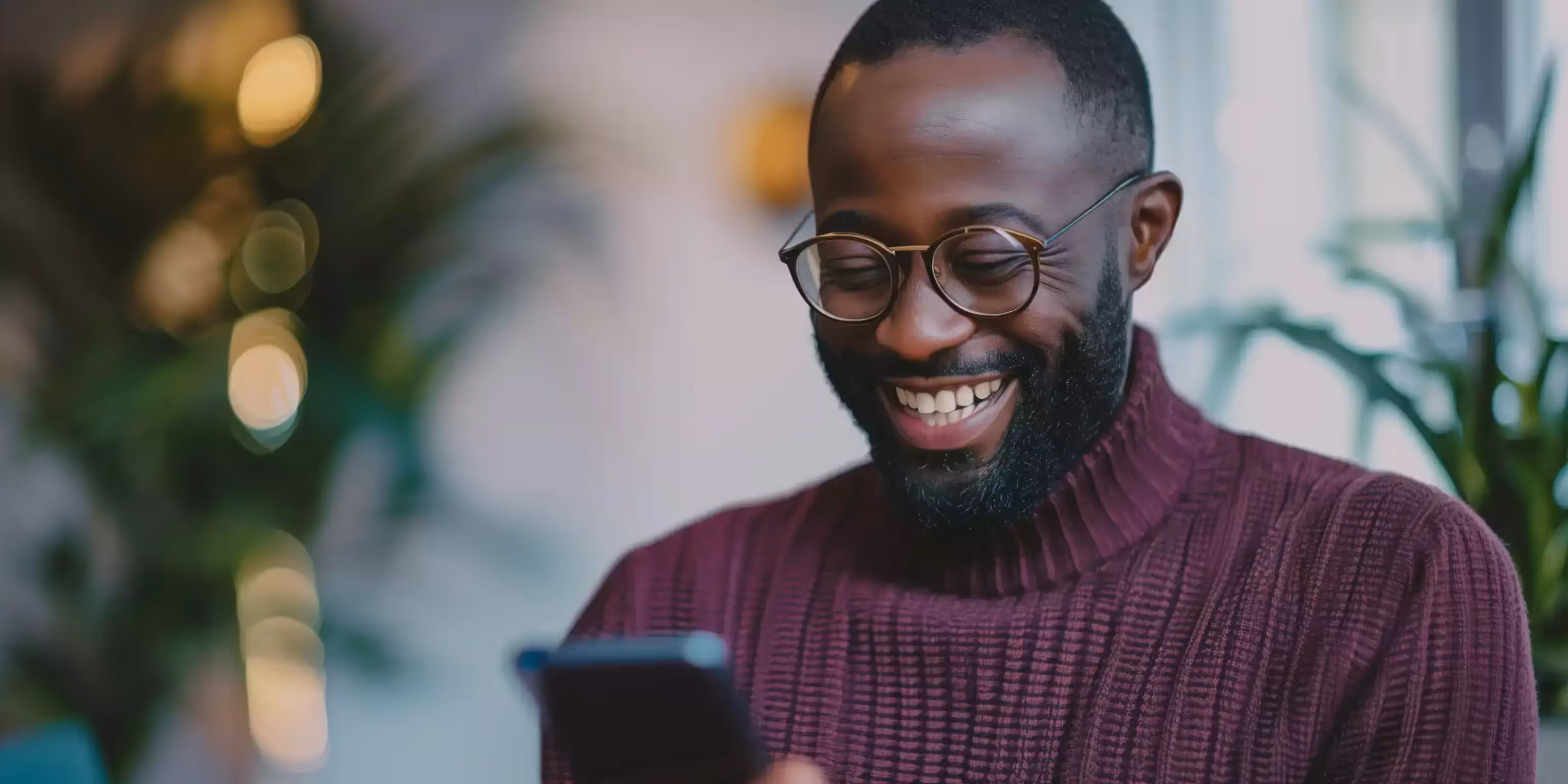 Imagem que ilustra artigo sobre como conquistar clientes com marketing digital mostra homem negro sorrindo, de óculos, vestindo malha roxa de gola alta, segurando o celular