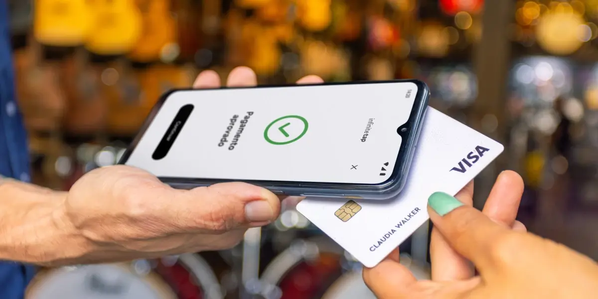 Celular vira maquininha com cartão sendo inserido e tela exibindo mensagem de pagamento aprovado.