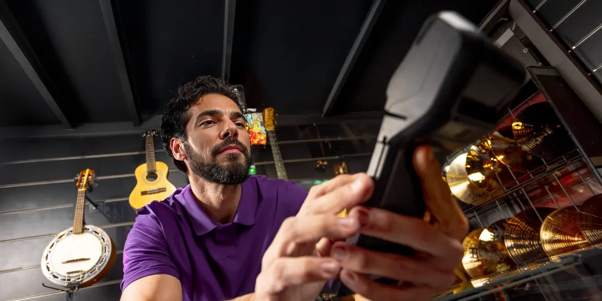 homem em sua loja de instrumentos musicais, com sua maquininha da InfinitePay nas mãos, utilizando-a após ler artigo dobre como usar a máquina de cartão.