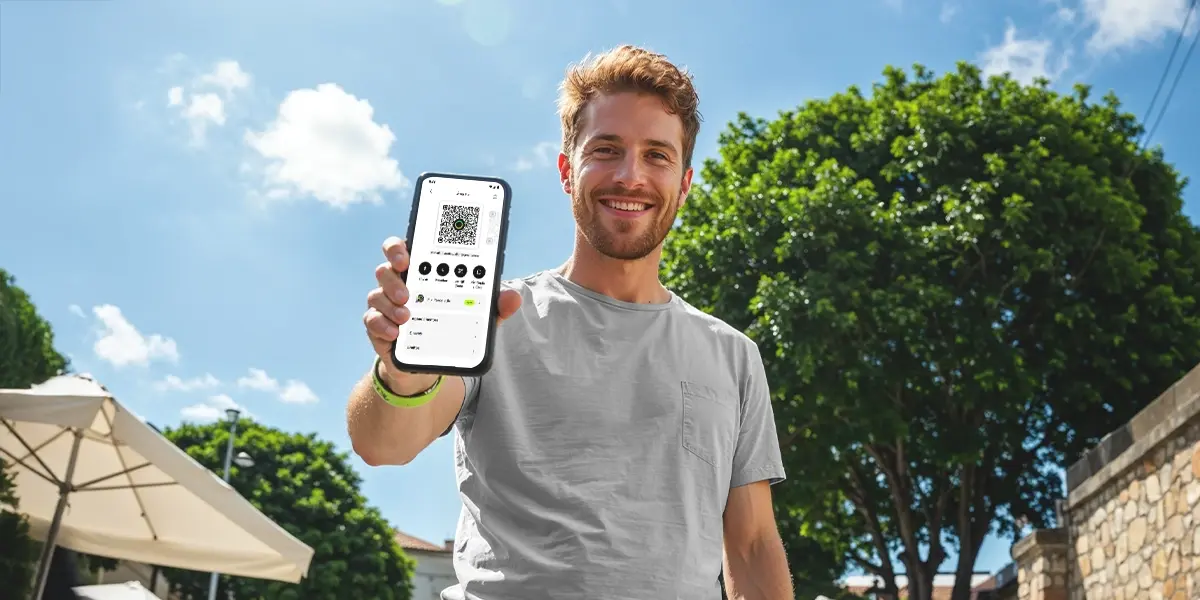 homem segurando seu smartphone em uma mao, mostrando-o para a camera. na tela do celular, mostra interface de um app processando um pix automatico.