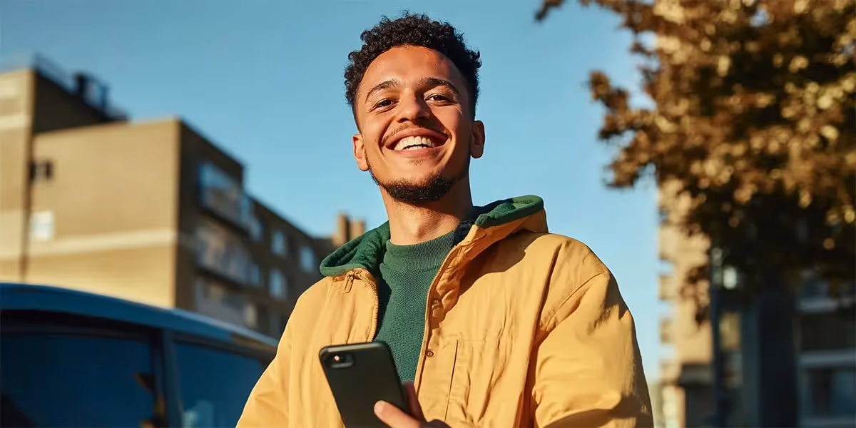 homem sorridente com celular na mão em uma rua ensolarada, transmitindo leveza e praticidade após ler sobre Pix Garantido