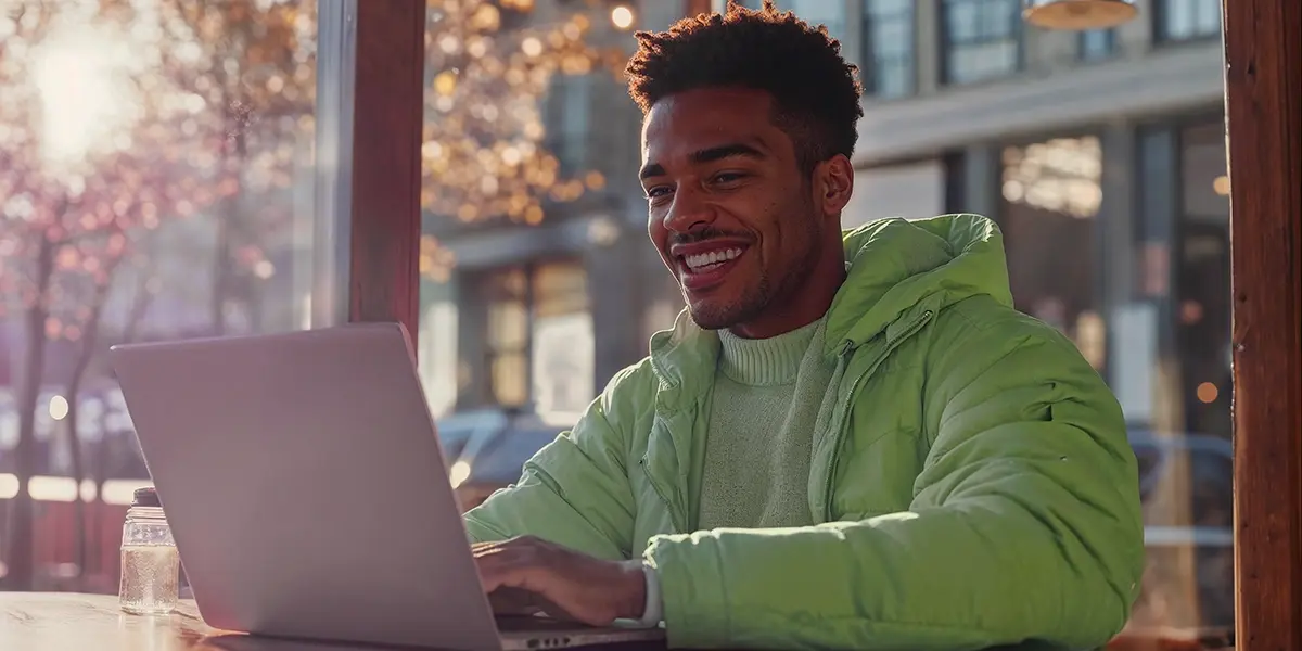 Homem sorrindo enquanto utiliza um laptop em ambiente externo, representando atividades relacionadas ao imposto de renda MEI.
