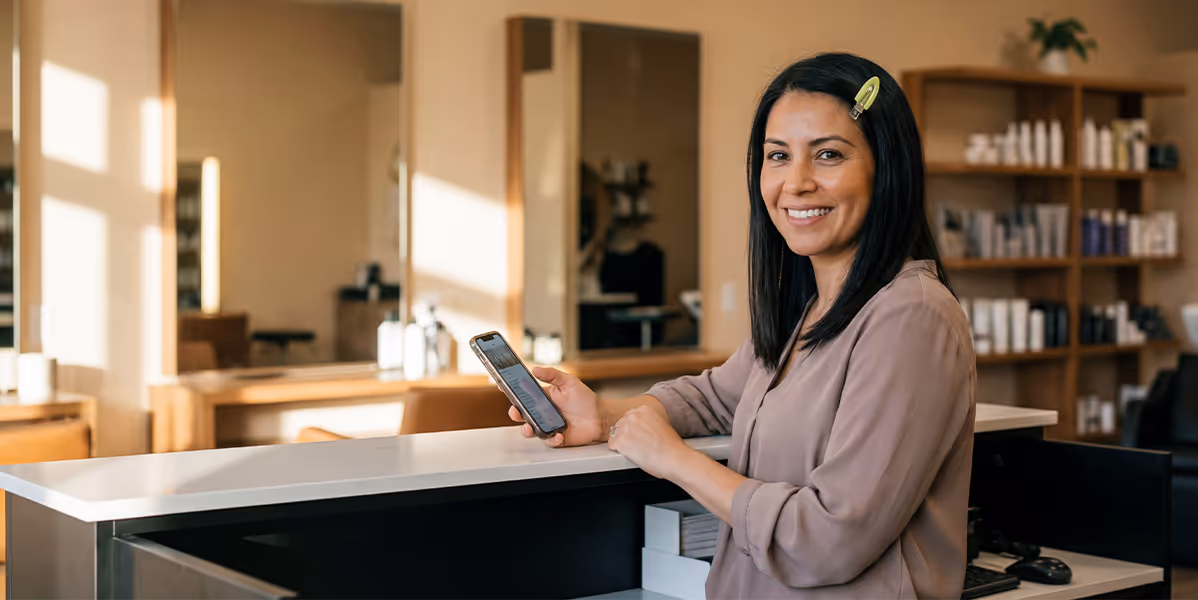 investimento cdb mulher sorridente segurando celular em um salão de beleza moderno.