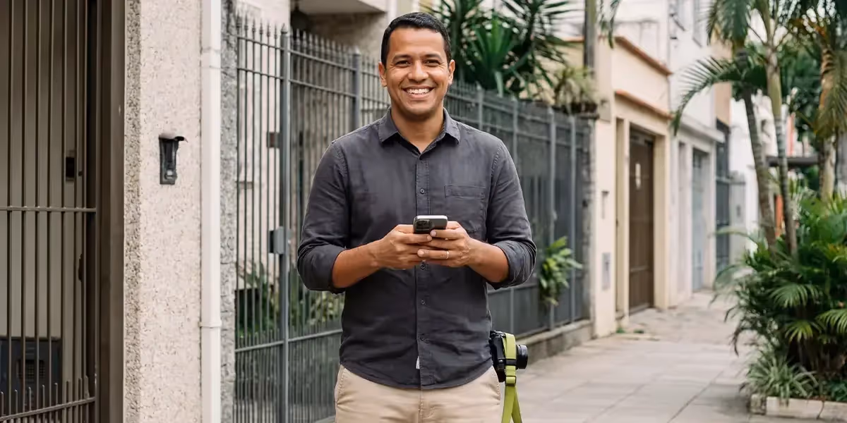 Homem sorridente usando celular na rua enquanto pesquisa se CDB tem FGC.