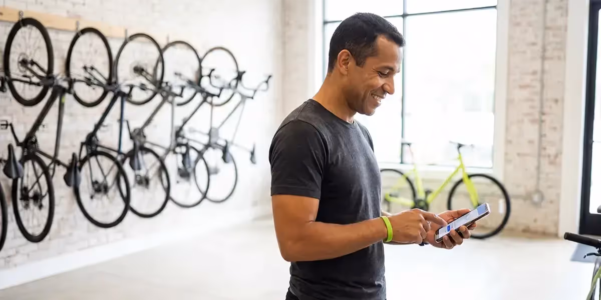 Homem em loja de bicicletas analisando opções de investimento em cdb ipca no celular.